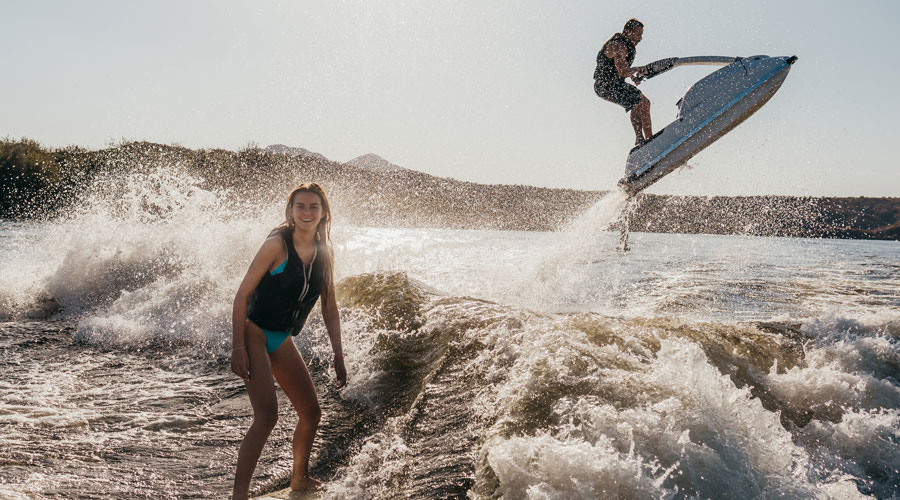 woman wake surfing and man jumping wake with jetski