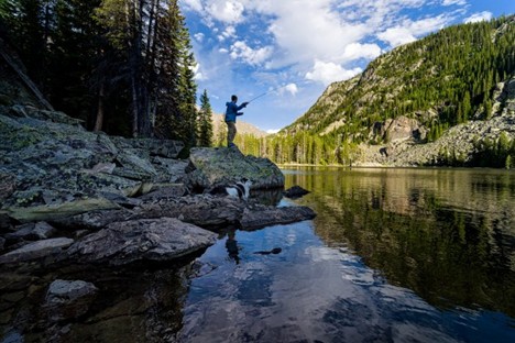 Person fishing at calm Colorado lake with forest and mountain view