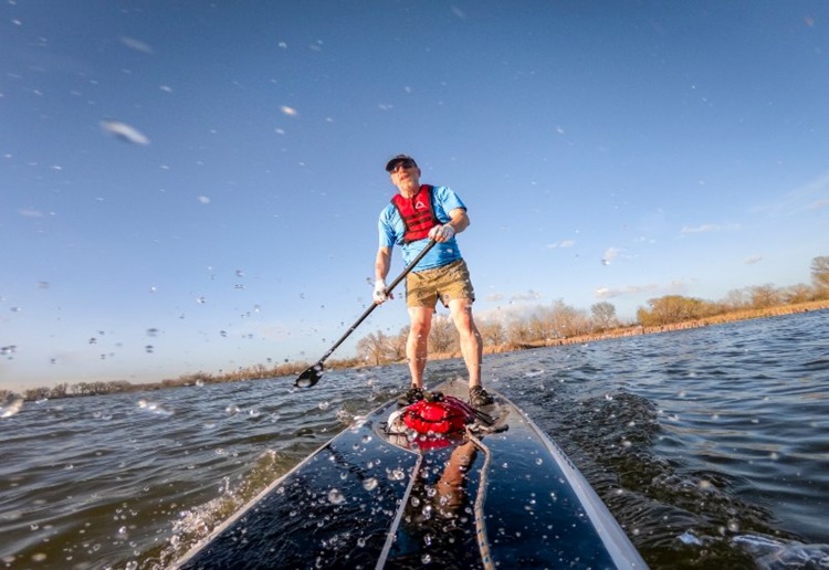 Person paddleboarding on Colorado lake with trees and blue sky